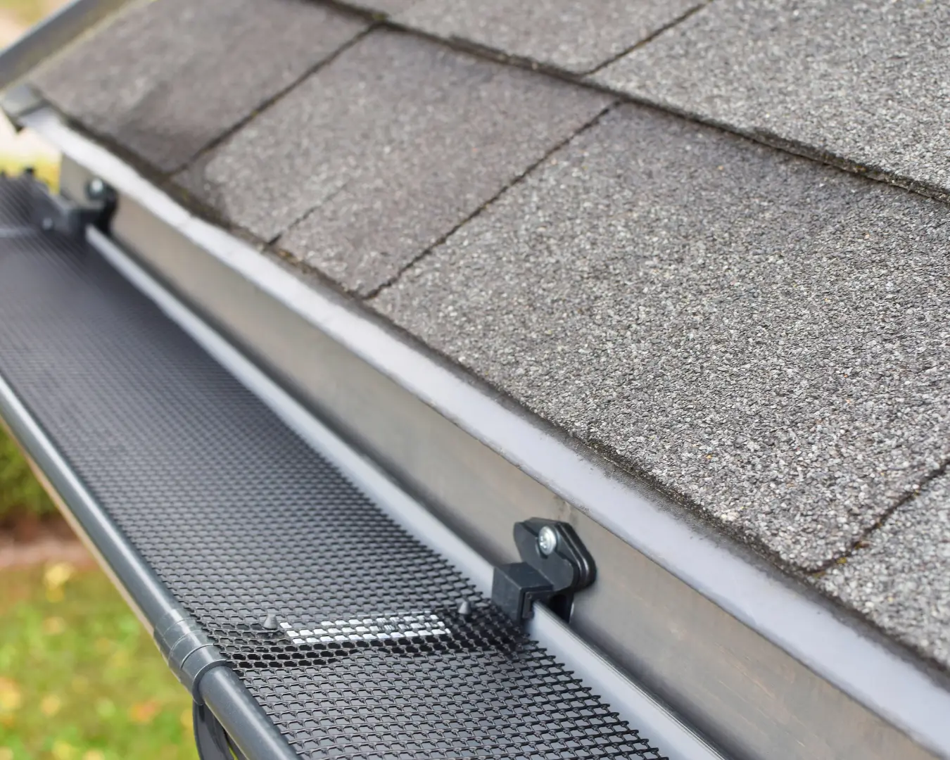 Close-up of a gutter guard installed on an asphalt shingle roofline
